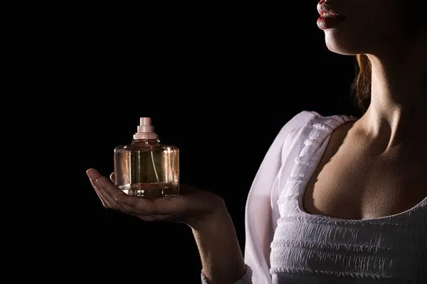 Beautiful woman holding bottle of perfume on black background