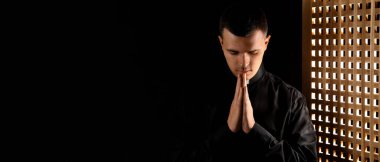 Young priest praying in confession booth. Banner for design clipart