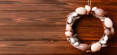 Tahta duvarda asılı yumurta ve tüylerden yapılmış Paskalya çelengi. Tasarım için pankart