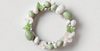 Beyaz duvarda asılı çiçekler, yumurtalar ve kelebeklerden oluşan Paskalya çelengi