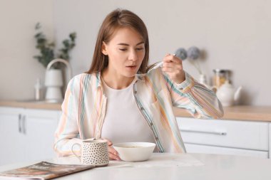 Beautiful woman eating soup with spoon at table in kitchen