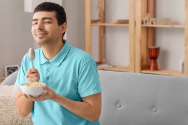 Evde kaşıklı ve mısır gevrekli genç bir adam var.