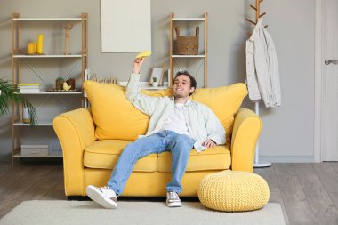 Evdeki kanepede kağıt uçakla oturan genç adam.