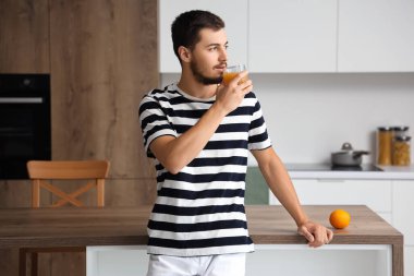 Genç adam mutfakta meyve suyu içiyor.