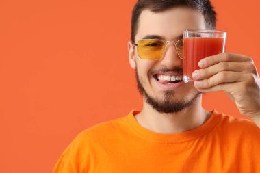 Kırmızı arka planda bir bardak meyve suyu olan genç adam, yakın plan.