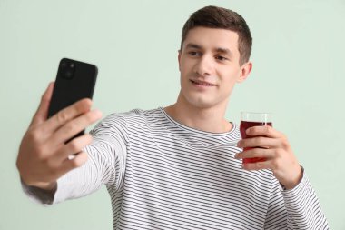 Elinde bir bardak meyve suyu olan genç adam yeşil arka planda selfie çekiyor, yakın plan.