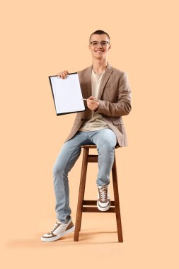 Turuncu arka planda sandalyede oturan yakışıklı genç iş adamı.