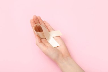 Woman with beige ribbon on pink background. Uterine cancer awareness concept