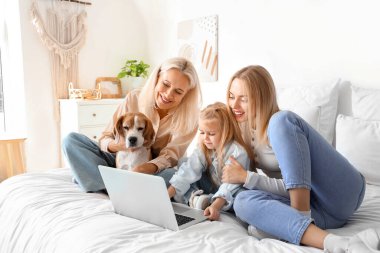 Yatak odasında dizüstü bilgisayar kullanan sevimli köpekli mutlu bir aile.