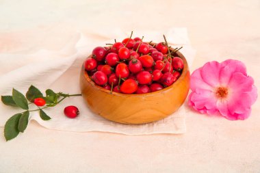 Taze gül kalçası böğürtlenli ahşap kase ve beyaz arka planda çiçek