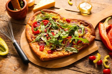 Lezzetli kalp şeklinde pizza ve ahşap arka planda malzemeler.