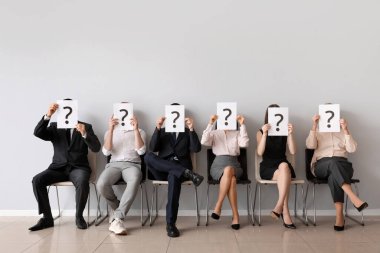 Adaylar, ışık duvarının yanında soru işaretleri olan kağıt kağıtlar tutuyorlar
