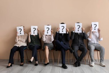 Adaylar, bej duvarın yanında soru işaretleri olan kağıt kağıtlar taşıyorlar