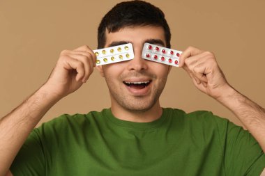 Bej arka planda A vitamini hapları olan genç adam, yakın plan.