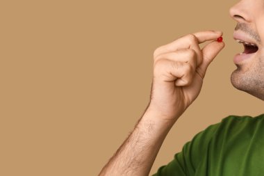 Genç adam bej arka planda A vitamini hapı alıyor, yakın plan.