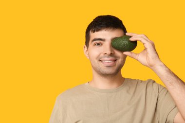 Avokado zengini sarı arka planda A vitamini zengini genç adam, yakın plan.