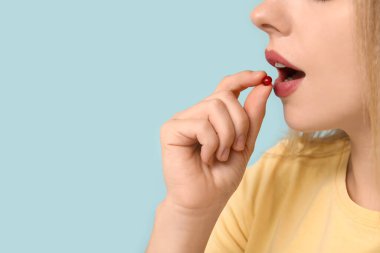 Genç bir kadın mavi arka planda A vitamini hapı alıyor, yakın plan.