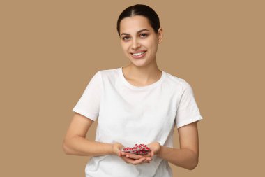 Bej arka planda A vitamini kapsülleri tutan genç ve güzel bir kadın.