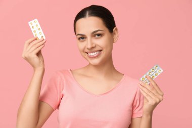 Güzel genç bir kadın pembe arka planda A vitamini kapsülleri tutuyor.