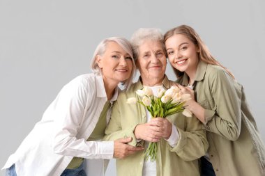 Annesi ve büyükannesiyle birlikte beyaz arka planda lale tutan genç bir kadın.