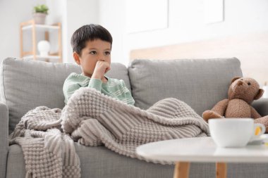 Evdeki kanepede öksüren küçük Asyalı çocuk.