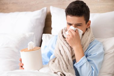 Yatak odasında hapşıran peçeteli hasta çocuk.