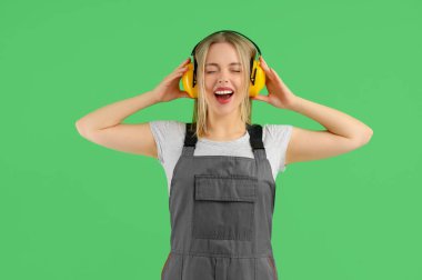 Yeşil arka planda koruyucu kulaklıkları olan kadın işçi.