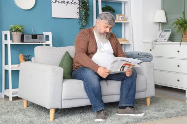 Oturma odasında gazete okuyan üzgün yaşlı adamın portresi.