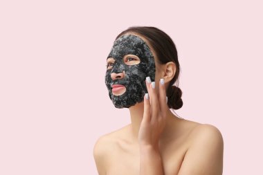 Yüzünde pembe arka planda aktif kömür maskesi olan genç bir kadın.