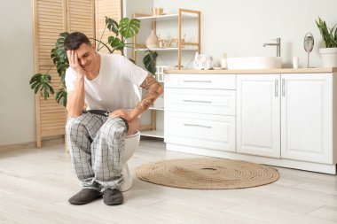 Hemoroidli genç adam tuvaletteki klozetin üzerinde oturuyor.