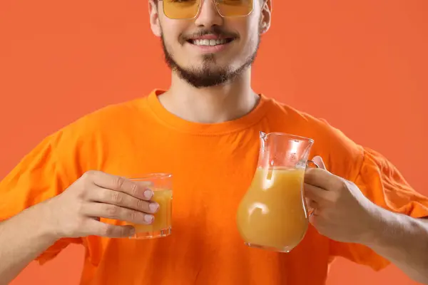 Young man with glass and jug of juice on red background, closeup