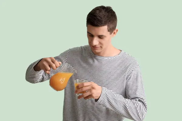 Young man pouring juice into glass on green background