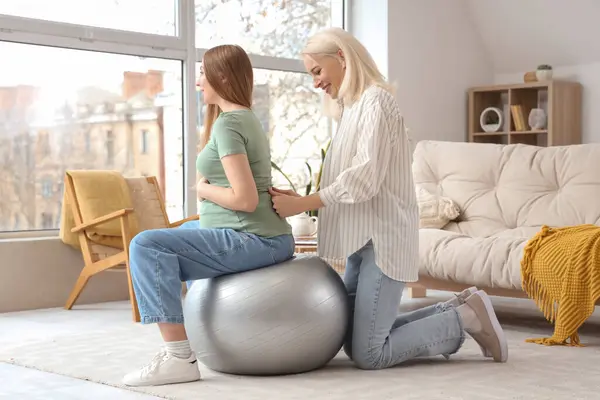 stock image Young pregnant woman with doula training on fitball at home