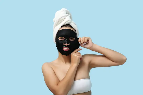 stock image Young woman with activated charcoal mask on her face against blue background