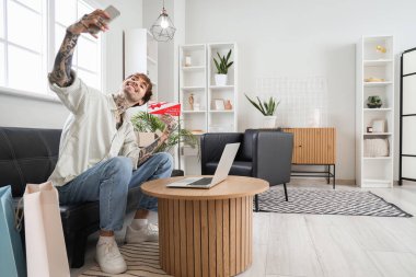 Hediye çeki ile evde selfie çeken dövmeli genç bir adam.