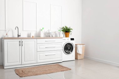 Lavabosu, çamaşır makinesi ve çamaşır sepetiyle aydınlatma odasının içinde.