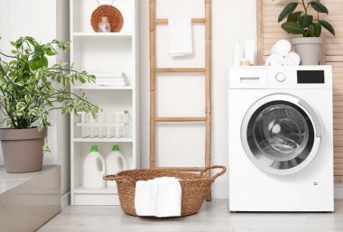 Sepetli modern çamaşır makinesi, raf ünitesi ve beyaz duvarın yanındaki giyinme ekranı. Ev çamaşır odasının içi.