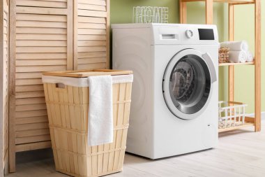 Sepetli modern çamaşır makinesi, raf ünitesi ve yeşil duvarın yanındaki giyinme ekranı. Ev çamaşır odasının içi.