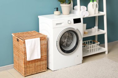Çamaşır sepeti, çamaşır makinesi ve raf ünitesi olan odanın içi.