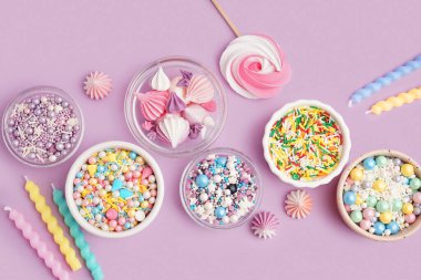 Rengarenk tatlı serpiştirilmiş kaseler ve leylak arkaplanda krema