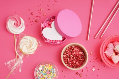 Renkli tatlı serpiştirilmiş kaseler, pembe arka planda krema ve dekor.