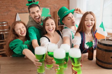 Group of young friends with beer celebrating St. Patrick's Day at table in pub