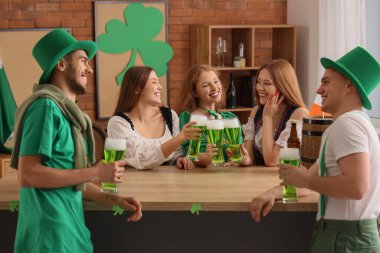 Group of young friends with beer celebrating St. Patrick's Day at table in pub