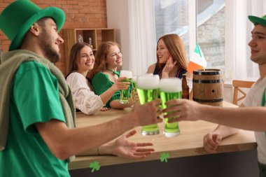Group of young friends with beer celebrating St. Patrick's Day at table in pub