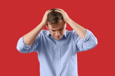 Kırmızı arka planda baş ağrısı çeken genç bir adam.