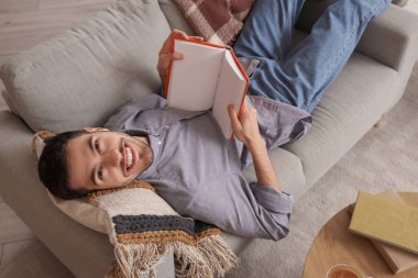 Evdeki kanepede kitap okuyan genç bir adam.