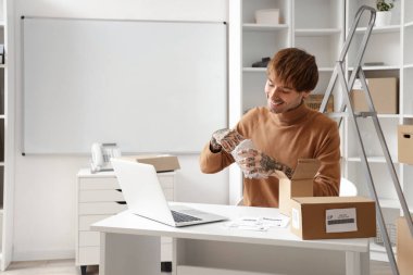 Depodaki masada müşteriler için paket paketleyen genç çevrimiçi mağaza satıcısı