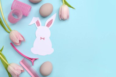 Paskalya yumurtalı kâğıt tavşan, lale ve mavi arka planda kuaför aksesuarları.