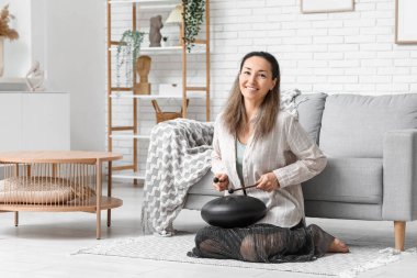 Evde sopalarla halıda glukofon çalan mutlu olgun kadın.