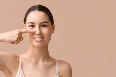 Bej arka planda burnunu gösteren gülümseyen genç bir kadın. Estetik ameliyat konsepti